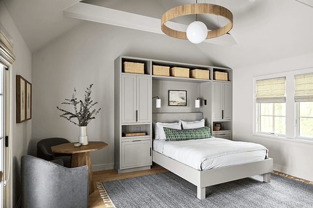 Bedroom in the poolhouse of a Mendham, NJ home, with a built-in headboard wall of cupboards and shelves and a woven ring light above