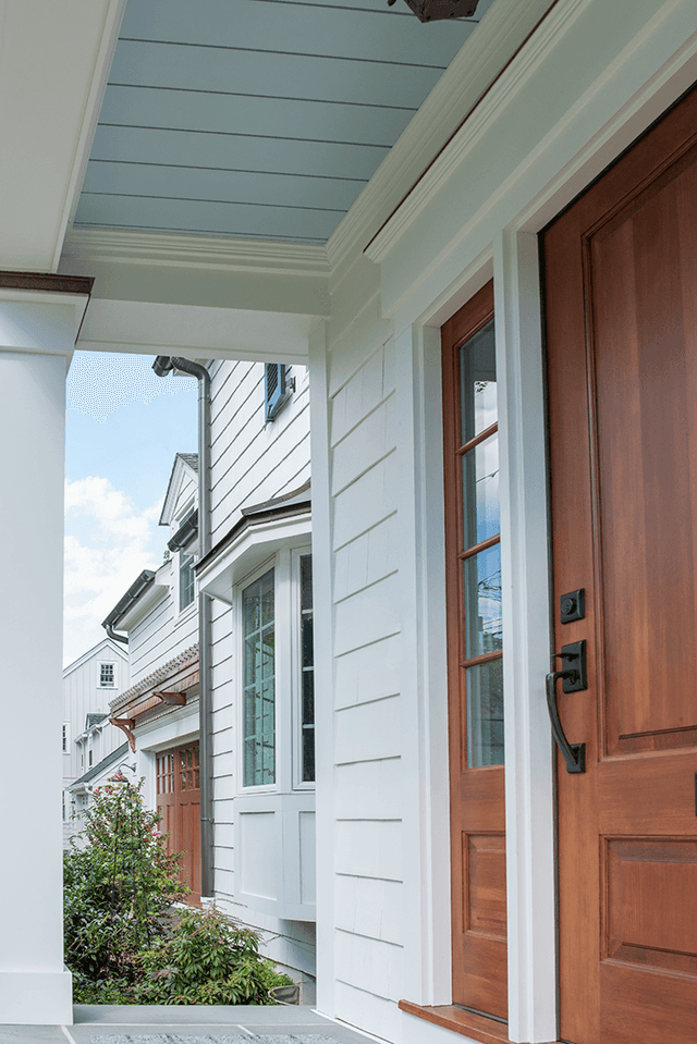 Angled view along the porch of a Westfield, NJ exterior renovation, with the blue-painted ceiling, the cedar door and white columns against the shingles