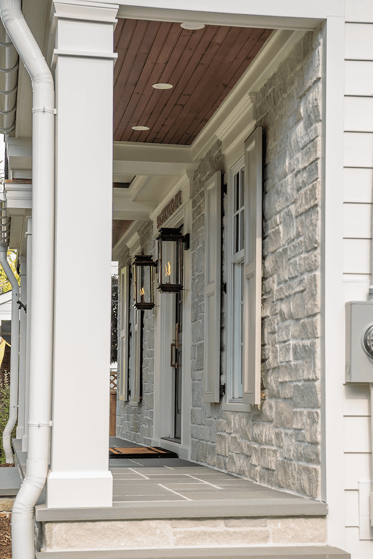 Porch of a Westfield, NJ home renovation looking down the colonnade, with a stained plank ceiling, gas lanterns and a stone wall
