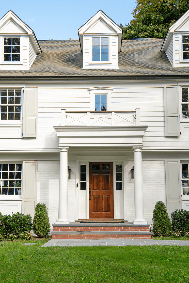 Front elevation of a Summit, NJ exterior remodel, with a pedimented portico over a wood door and sidelights, dormers above and clipped boxwood either side