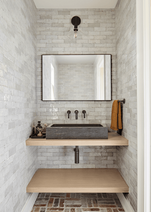 Powder room off the mudroom of a Mendham, NJ home, lined in handmade tile with a stone trough basin on an oak shelf and a brick floor
