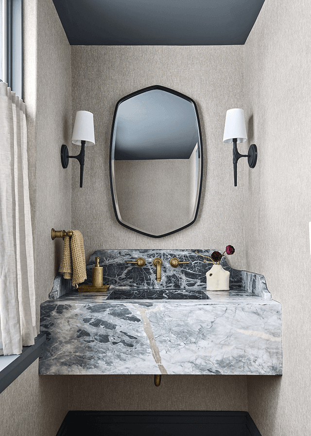 Floating marble basin with brass taps under a hexagonal mirror between two sconces in a Mendham, NJ powder room