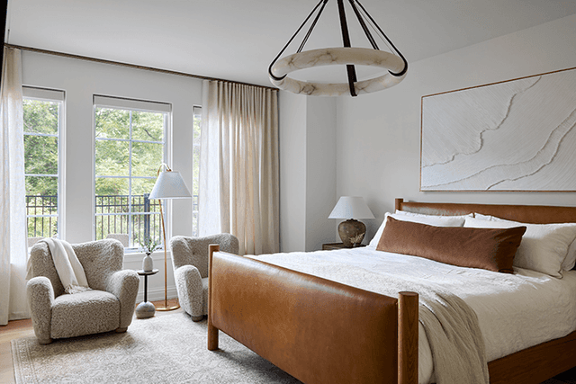 Primary bedroom of a Mendham, NJ home with a leather sleigh bed, two armchairs at the window and a black iron ring chandelier