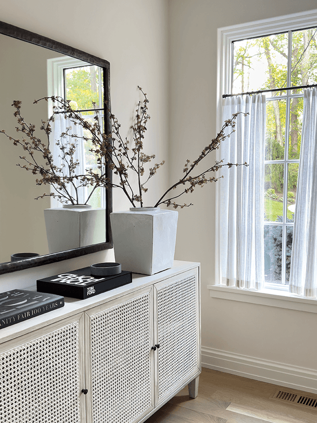 Anteroom to the primary suite of a Mendham, NJ home, with a cane-fronted console under a large leaning mirror between two windows