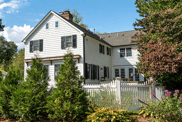 Side of a Westfield, NJ exterior renovation across the garden, with black shutters, a picket fence and flowering borders in front