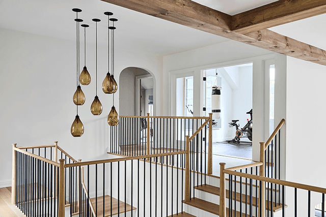 Stairwell of a Mendham, NJ home seen from the landing, with oak handrails, black balusters and amber glass pendants dropping through the void