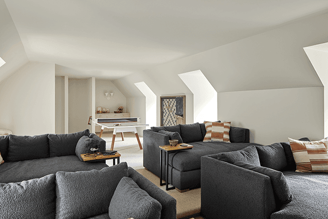 Home theater in a Mendham, NJ home under a sloped ceiling, with two charcoal sectionals facing the screen and a games table behind
