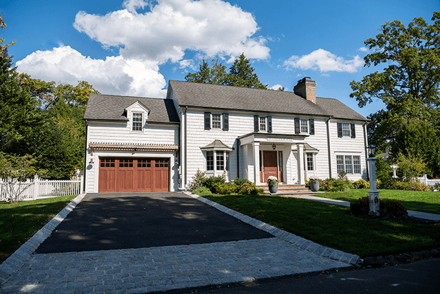 Wide view of a Westfield, NJ home remodel from the street, with cedar garage doors, white siding and a long blacktop drive