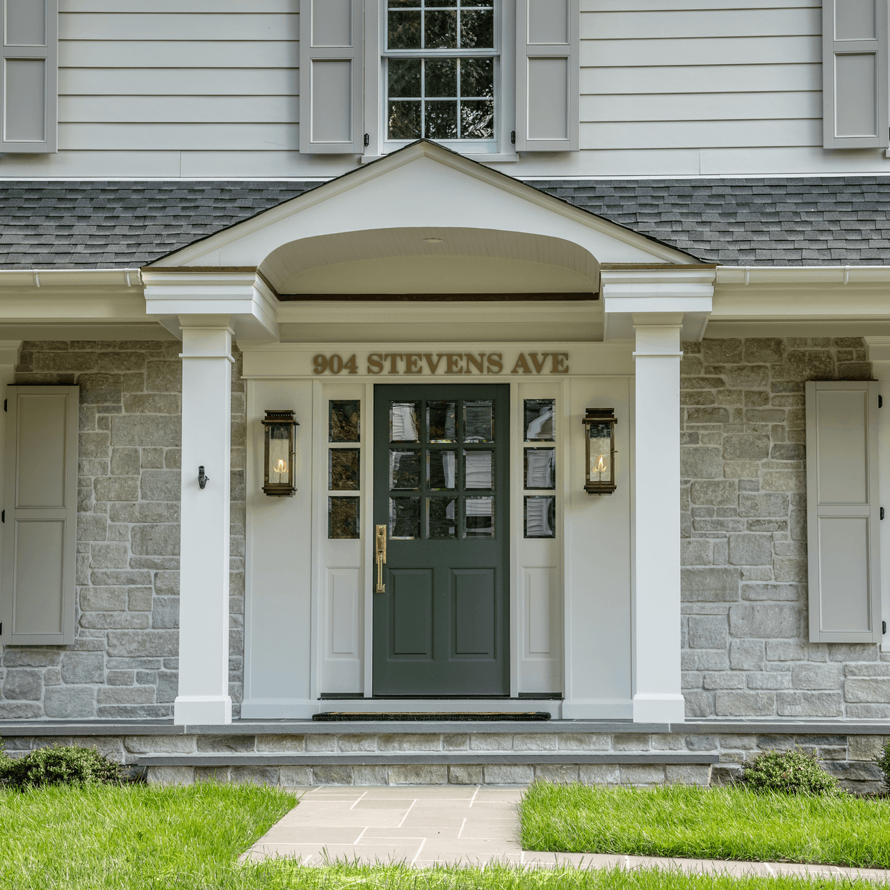 Portico entry with a deep green front door, brass hardware, gas lanterns and gray stone veneer in Westfield, NJ