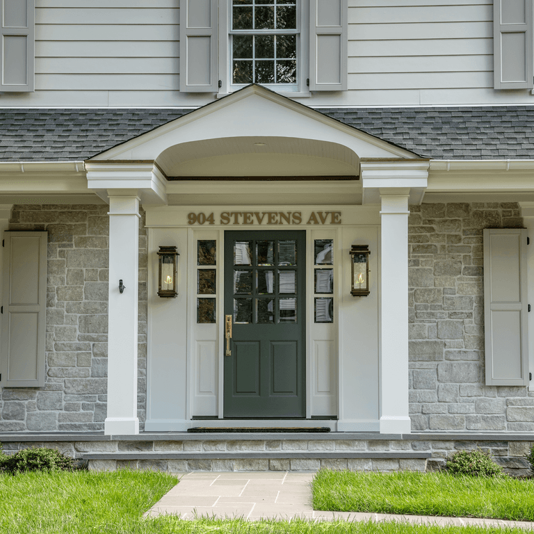 Portico entry with a deep green front door, brass hardware, gas lanterns and gray stone veneer in Westfield, NJ