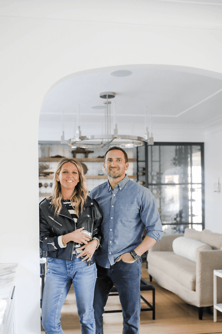 Mike and Ellie Mroz under an arched cased opening in a Westfield, NJ home, with a ring chandelier and steel-framed glass doors behind them