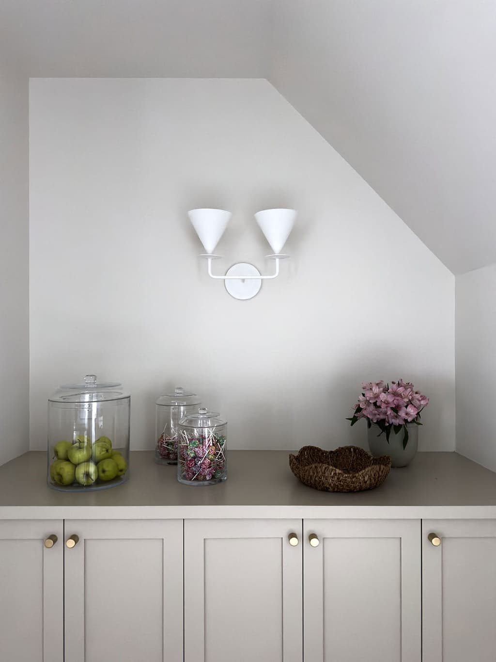 Built-in cabinetry fitted under a sloped attic ceiling, with brass knobs, a stone counter and a two-arm white sconce on the wall above