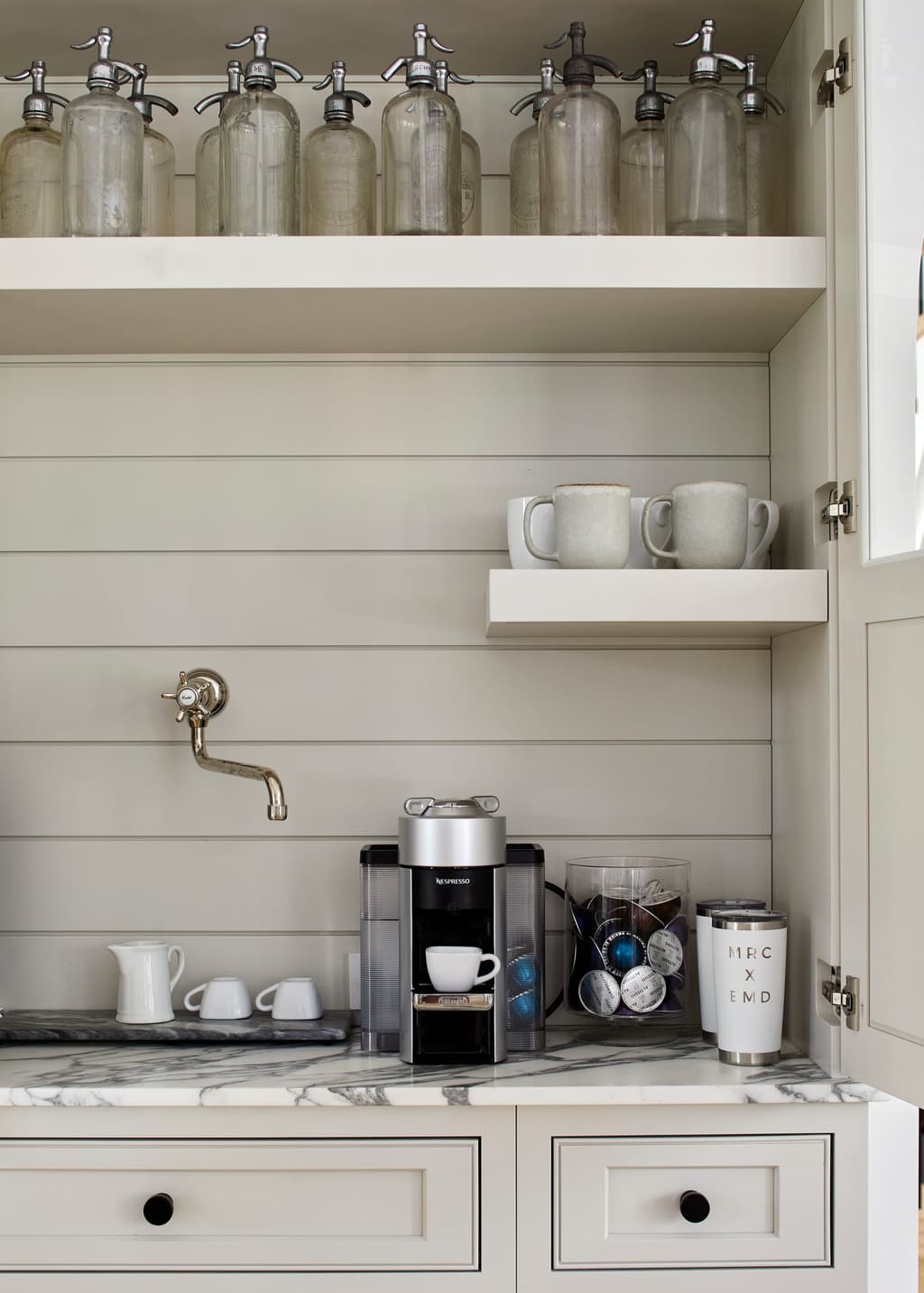 Coffee station set into cabinetry, with a marble counter, glass storage jars on open shelves and a brass tap