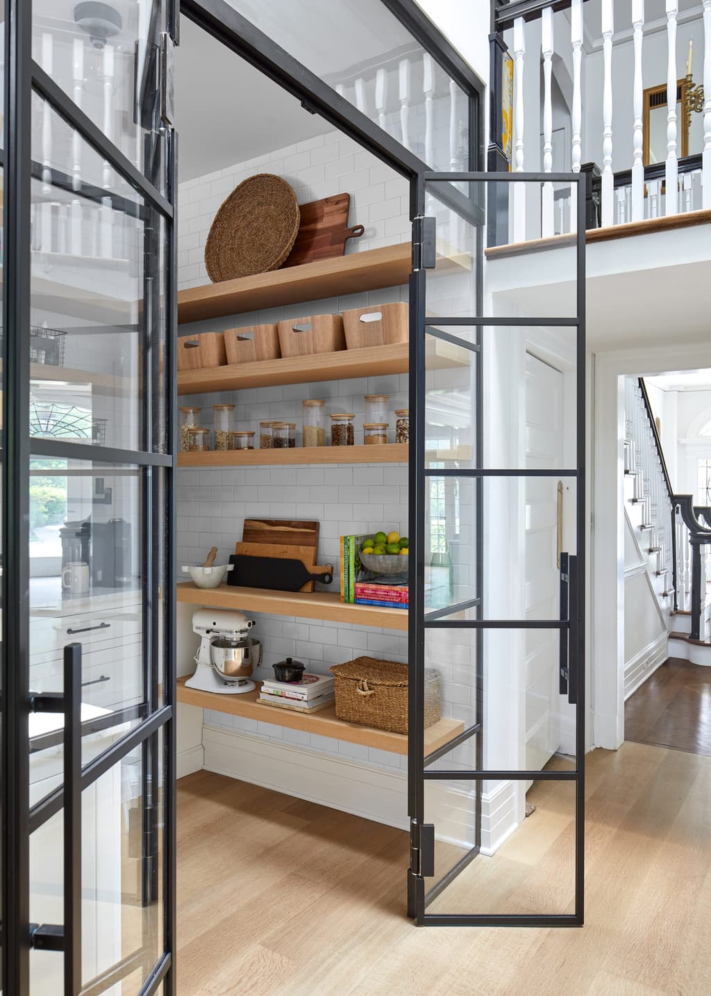Walk-in pantry behind black steel and glass doors in a historic Westfield, NJ home, with floating oak shelves and a counter run along the back wall