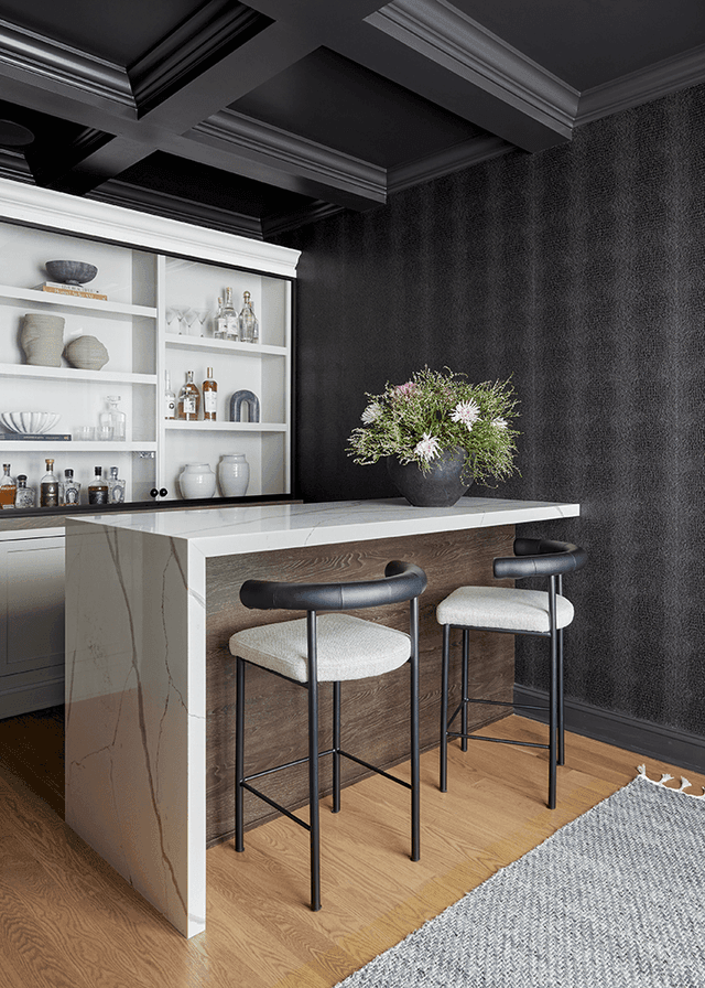 Bar in a Westfield, NJ custom home, with dark textured walls, a beamed ceiling, pale custom cabinetry and a stone counter with upholstered stools
