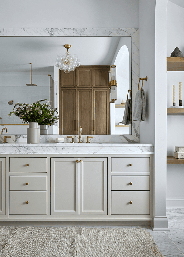 Double vanity with a thick marble top, brass fittings and an arched wood door beyond, in a Westfield, NJ custom home bathroom