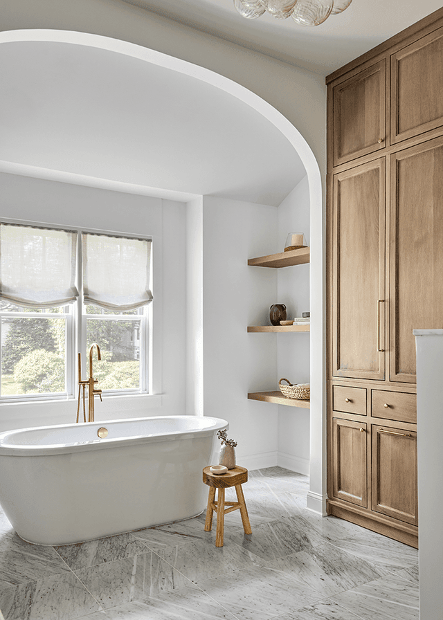 Freestanding tub in an arched plaster alcove beside custom oak cabinetry and open shelves in a Westfield, NJ new-construction home, with a brass floor-mounted filler