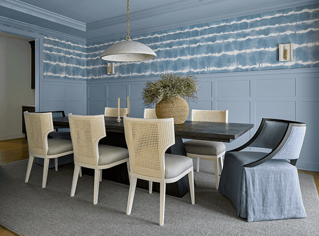 Dining room in a Westfield, NJ custom home, with blue patterned wallpaper, wainscoting, slipcovered chairs and a long table under a globe pendant
