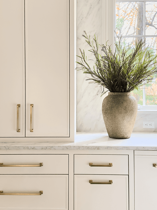 Custom kitchen cabinetry in a Summit, NJ remodel, with long brass pulls, a marble counter and a marble slab carried up the wall