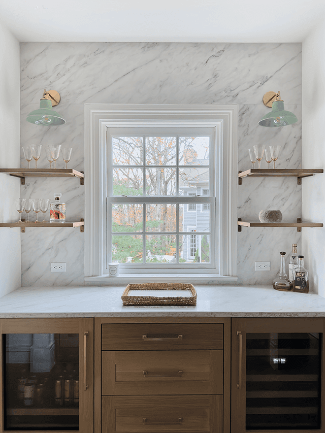 Pantry window wall in a Summit, NJ renovation, with a marble slab backsplash, glass shelves on brass brackets and a wine refrigerator in the walnut base run