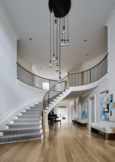Double-height foyer of a Summit, NJ renovation, with a curved staircase, a cascading pendant through the stairwell and a grand piano beyond
