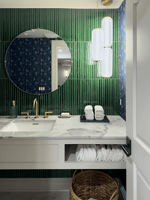 Powder room in a Summit, NJ remodel, with a green fluted tile wall, a round mirror, a brass tap and a marble top over open towel storage
