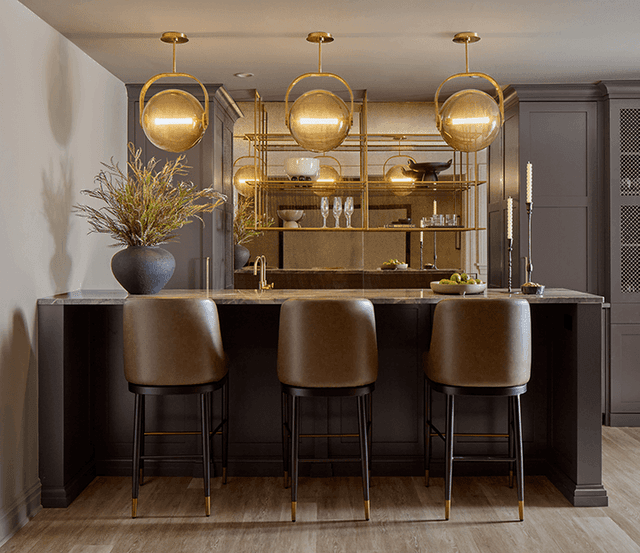 Home bar in a Summit, NJ renovation, with leather stools at a dark counter, a brass-lined back bar and three globe pendants above