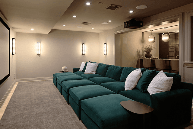 Home theater in a Summit, NJ renovation, with a deep green sectional facing the screen and sconces down both walls