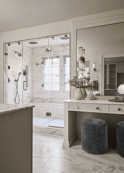 Marble bathroom in a Summit, NJ renovation, with a glass shower, a built-in dressing table and a round upholstered stool