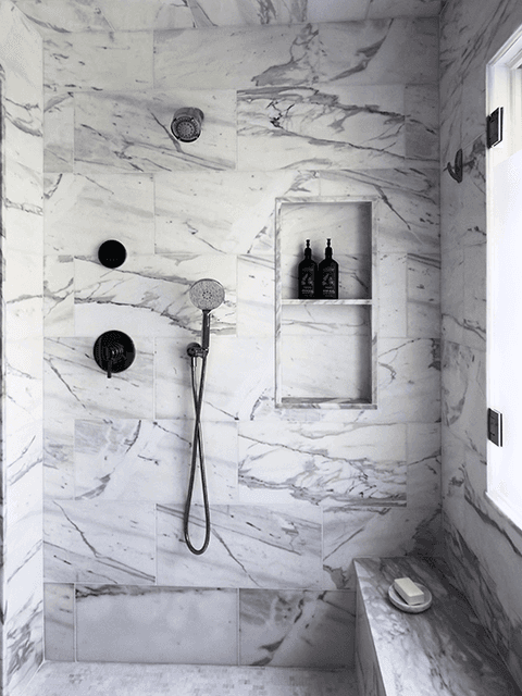 Shower lined in bookmatched marble in a Summit, NJ bathroom, with a recessed niche and black fittings
