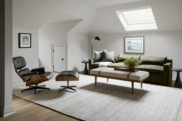 Sitting end of a Summit, NJ home office under a sloped ceiling with a skylight, with a leather lounge chair, a green sofa and a bench on a pale rug