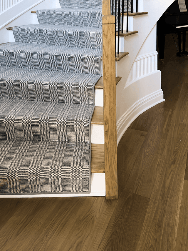 Stair of a Summit, NJ home remodel, with a fluted curved skirt, an oak handrail on slim metal balusters and a patterned runner