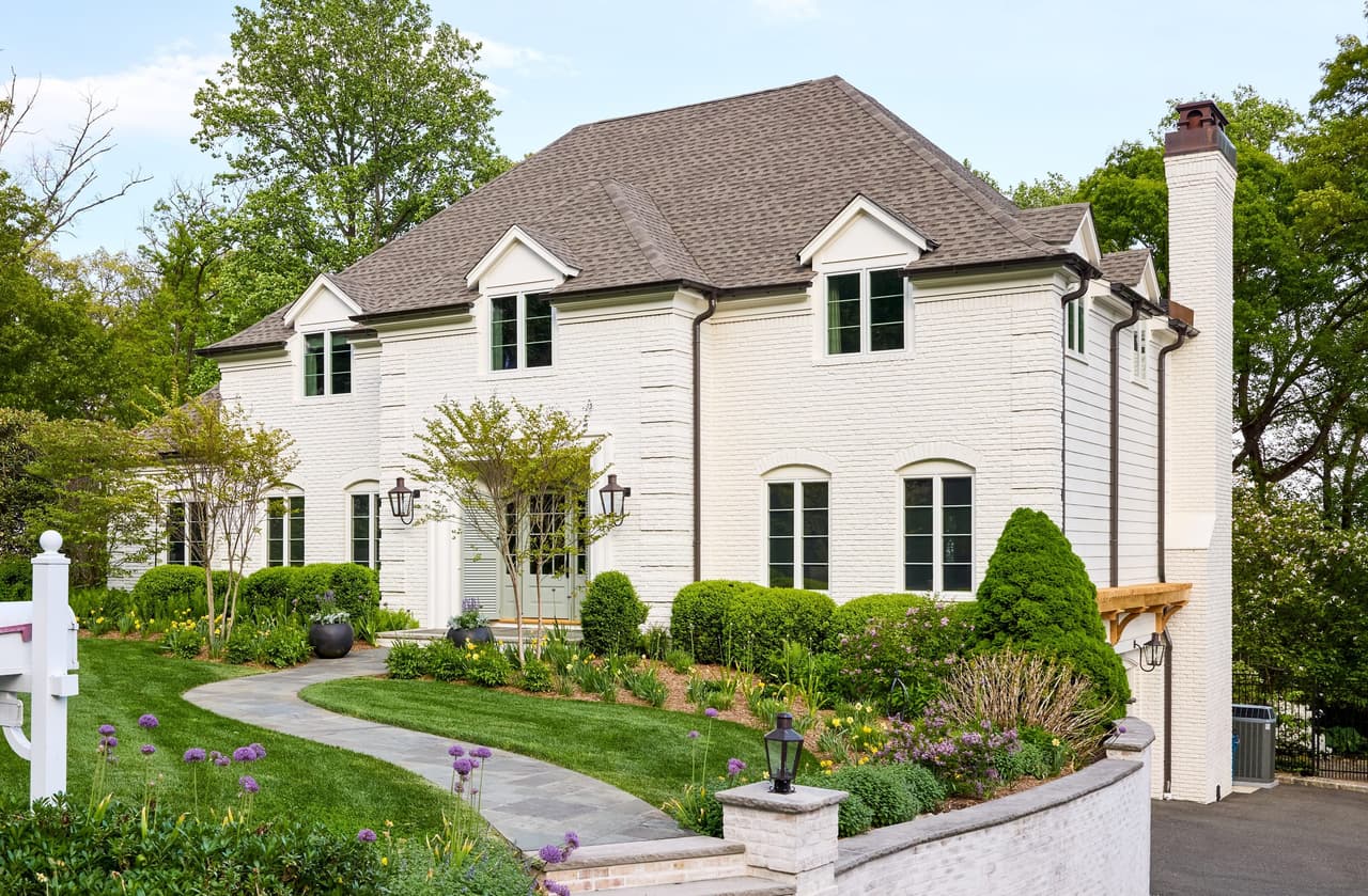 Angled view of a painted white brick home with gabled dormers, a copper-capped chimney, gas lanterns and a bluestone walkway in Mountainside, NJ