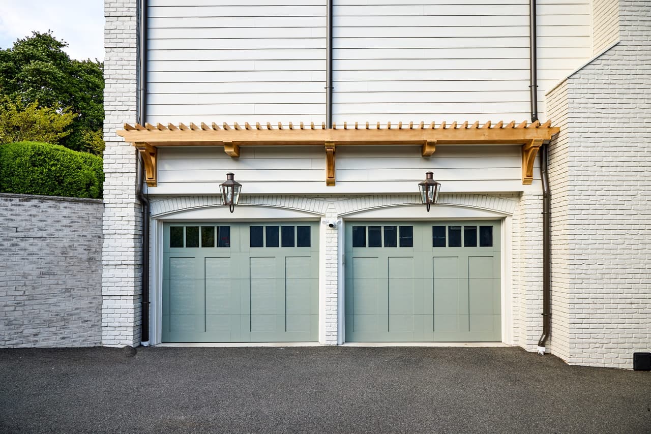 Pair of blue-green carriage garage doors under a cedar trellis and two lanterns at a Mountainside, NJ home, built by Michael Robert Construction