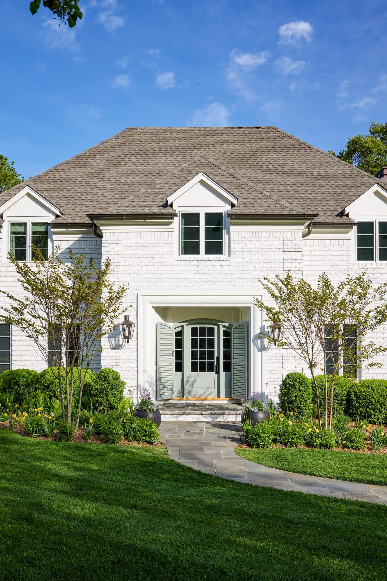 Blue-green front door with sidelights and louvered shutters at a painted brick home in Mountainside, NJ, reached by a curving walk across the lawn