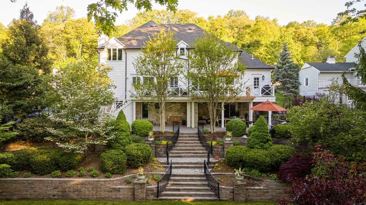 Back of a Mountainside, NJ home across the garden, with a stone lower storey, a covered patio below a screened porch and stone steps up through the planting