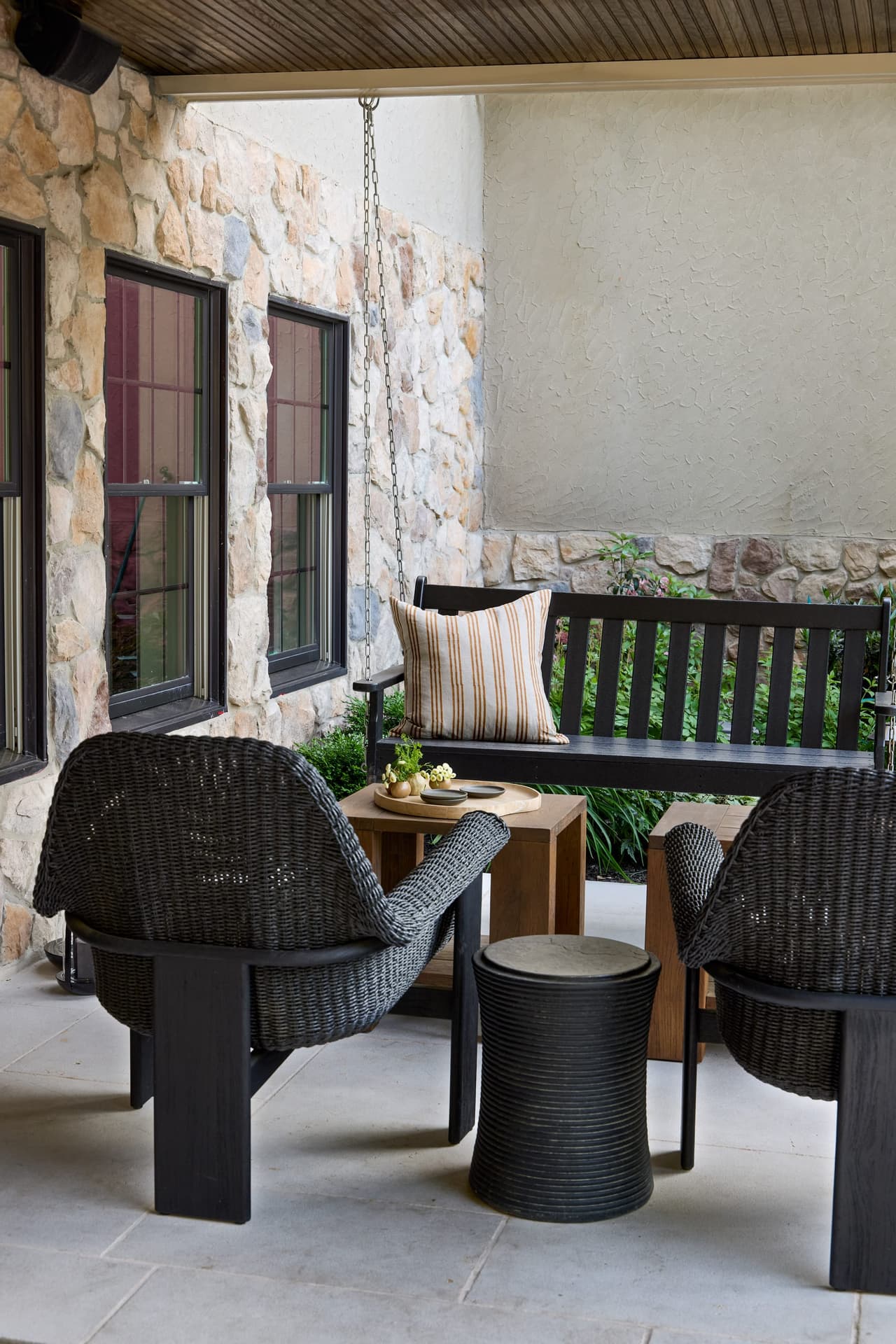 Covered porch in Westfield, NJ with natural stone walls, a wood ceiling, large-format stone flooring and a suspended porch swing, built by Michael Robert Construction