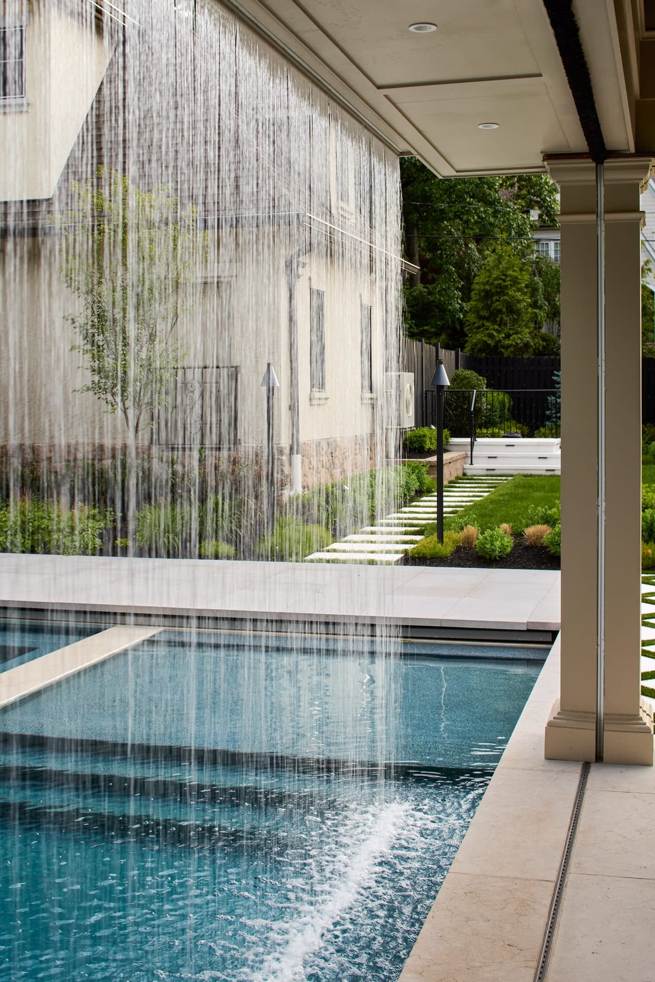 Custom swimming pool with architectural waterfall curtain and covered outdoor living cabana pavillion built by Michael Robert Construction in a indoor and outdoor living project in Westfield, NJ