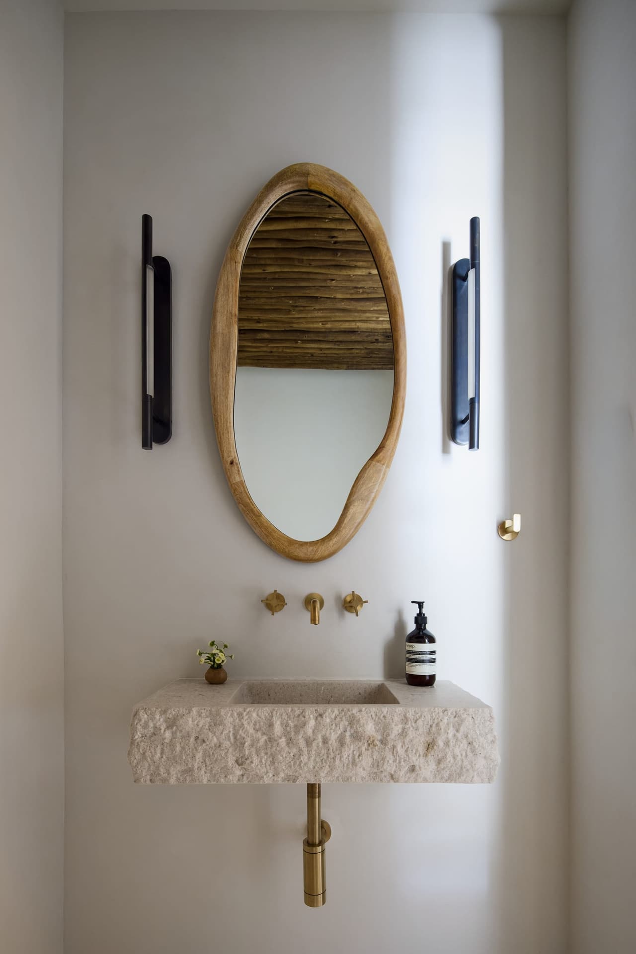 Luxury pool house bathroom featuring a floating carved stone sink wall mounted brass plumbing and custom architectural lighting in a indoor and outdoor living project in Westfield, NJ