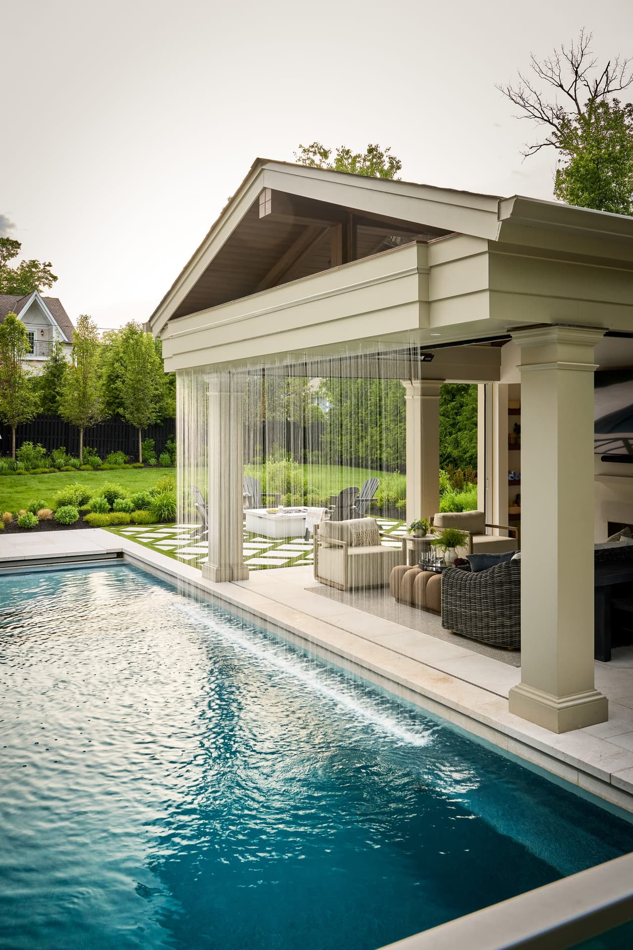 Side view of an integrated rain curtain water feature cascading from a custom covered NJ pool pavilion into a luxury swimming pool in a indoor and outdoor living project in Westfield, NJ