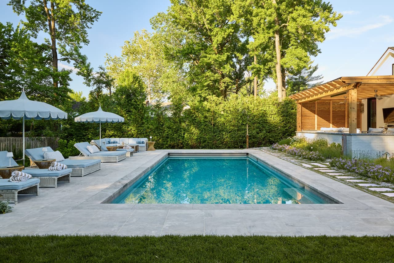 Long view across a rectangular pool to loungers, umbrellas and a cedar pergola in a Westfield, NJ backyard