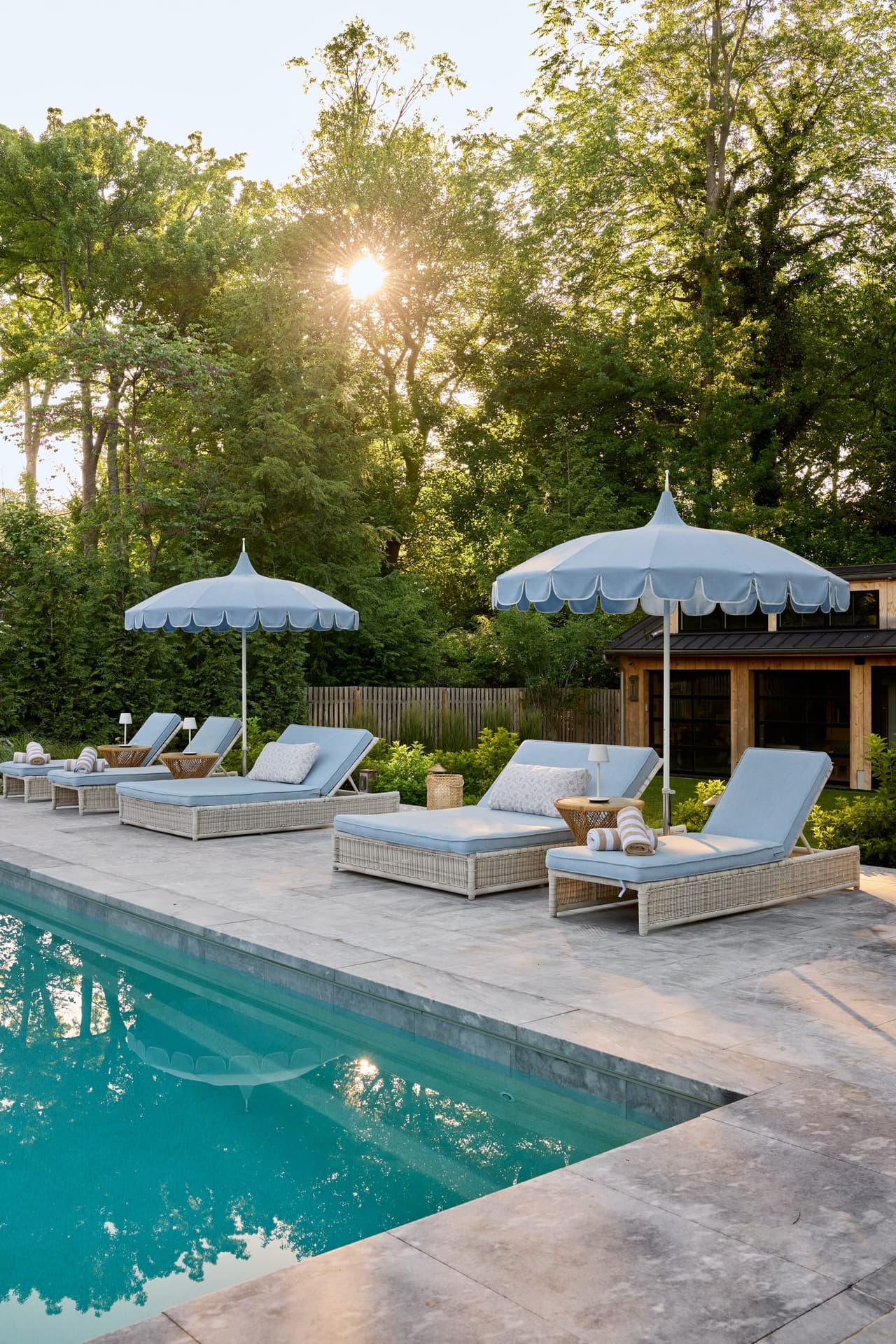 Poolside chaises with blue cushions under scalloped umbrellas beside the pool of a Westfield, NJ custom home