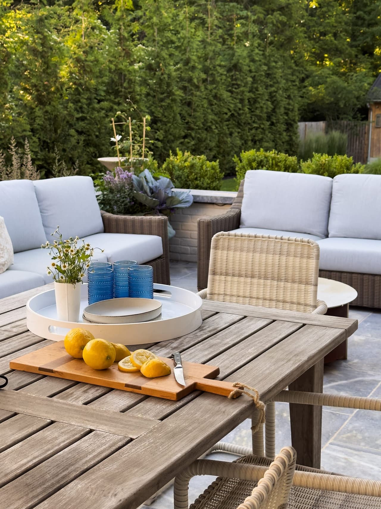 Teak sectional and low table on the stone patio of a Westfield, NJ new-construction home, set with ceramics and a board of lemons