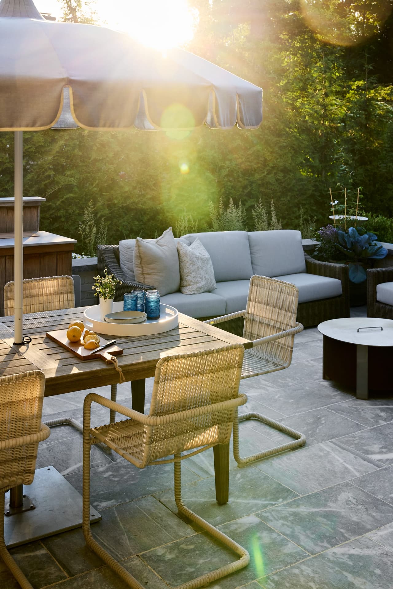 Patio dining in woven and teak beside lounge seating at a Westfield, NJ new-construction home, in low evening sun