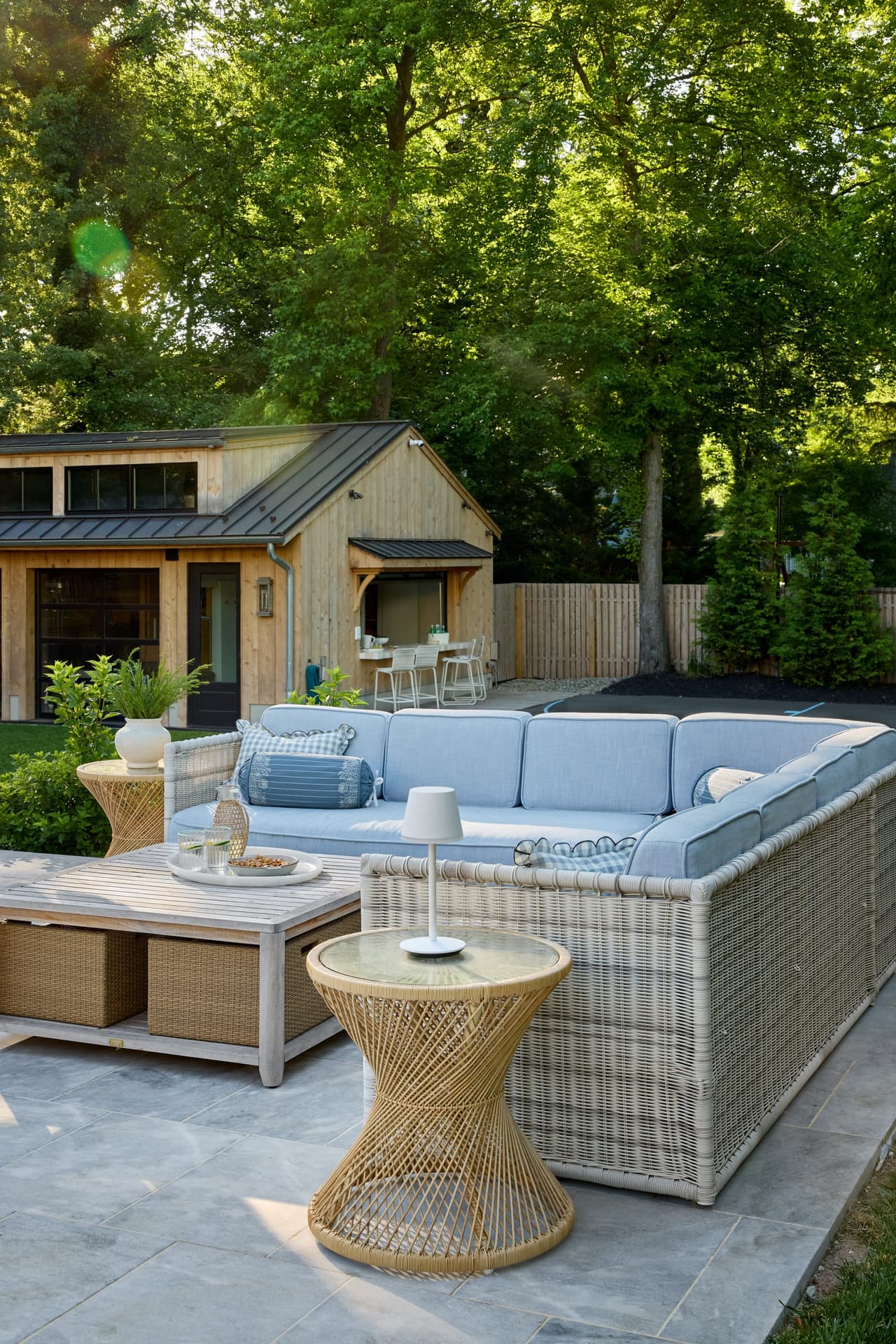 Poolside lounge with a cushioned sofa and woven side table in front of the cedar pool house at a Westfield, NJ home