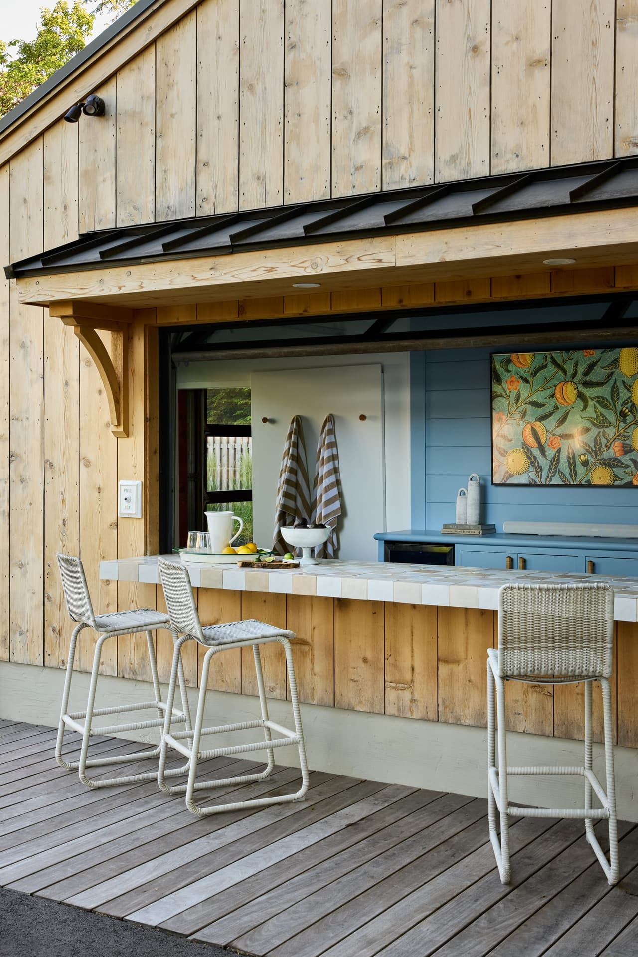 Pass-through bar of a Westfield, NJ pool house, with vertical cedar siding, a tiled counter, light blue cabinetry and metal counter stools