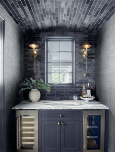 Bar alcove with navy cabinetry, a marble counter, a glazed tile back wall and paired sconces