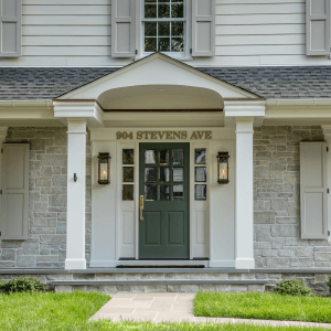 Portico entry with a deep green front door, brass hardware, gas lanterns and gray stone veneer in Westfield, NJ