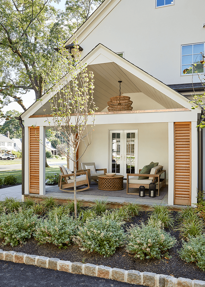 Gabled side porch of a Westfield, NJ renovation seen from the lawn, with cedar louvered shutters either side and a planted border across the front